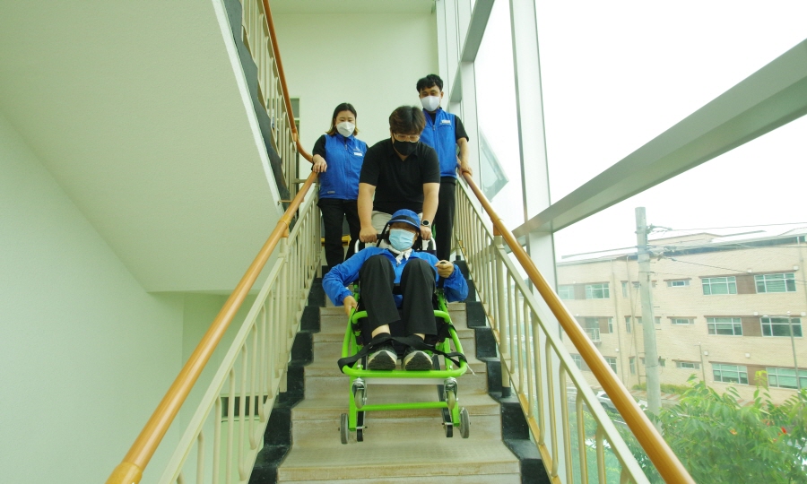 응급환자를 3명의 직원이 계단으로 이송 가능한 장비에 응급환자를 실어 계단을 내려오는 모습입니다.